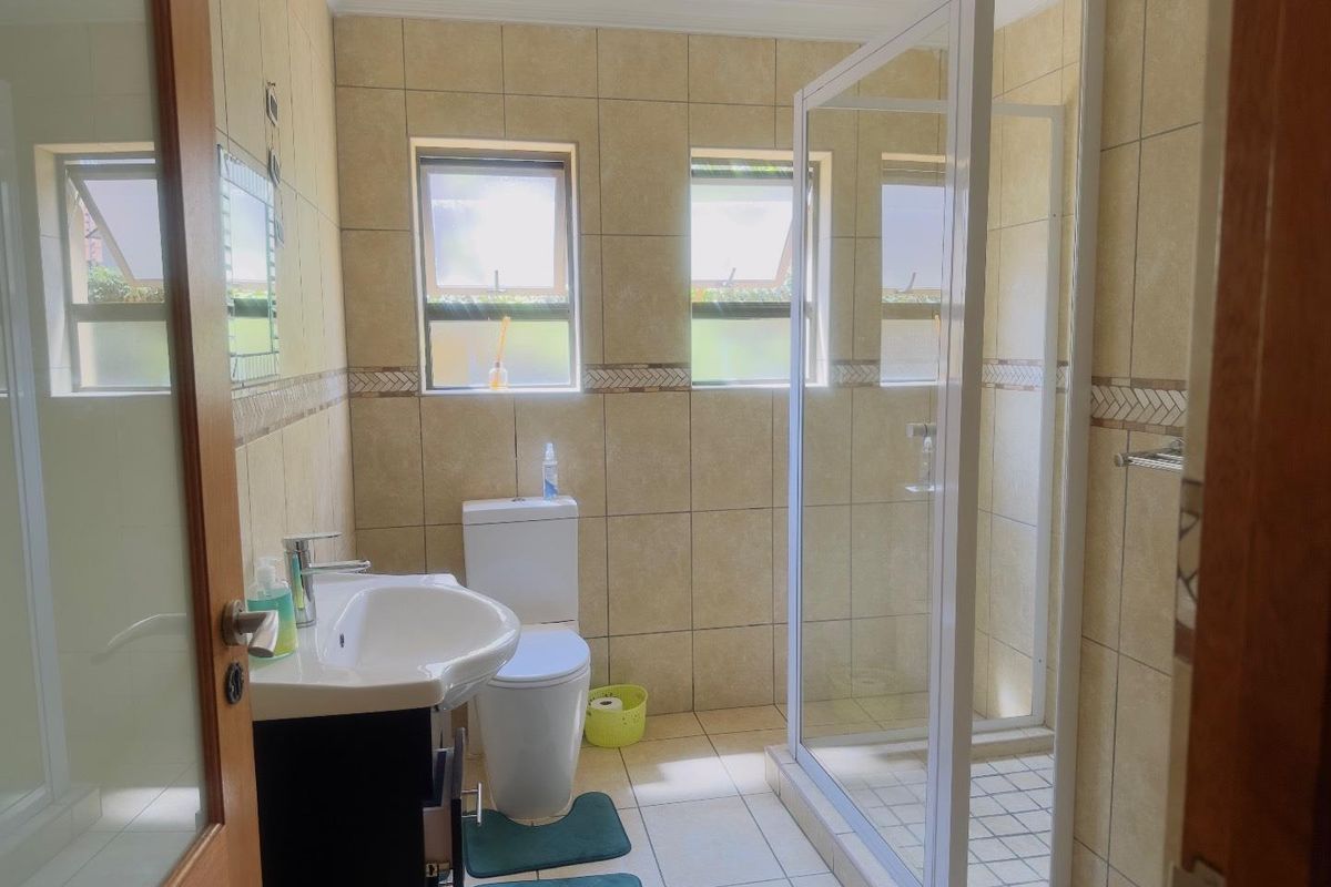 A functional bathroom featuring a glass-enclosed shower, a pedestal vanity, and a toilet, finished with neutral wall and floor tiling.
