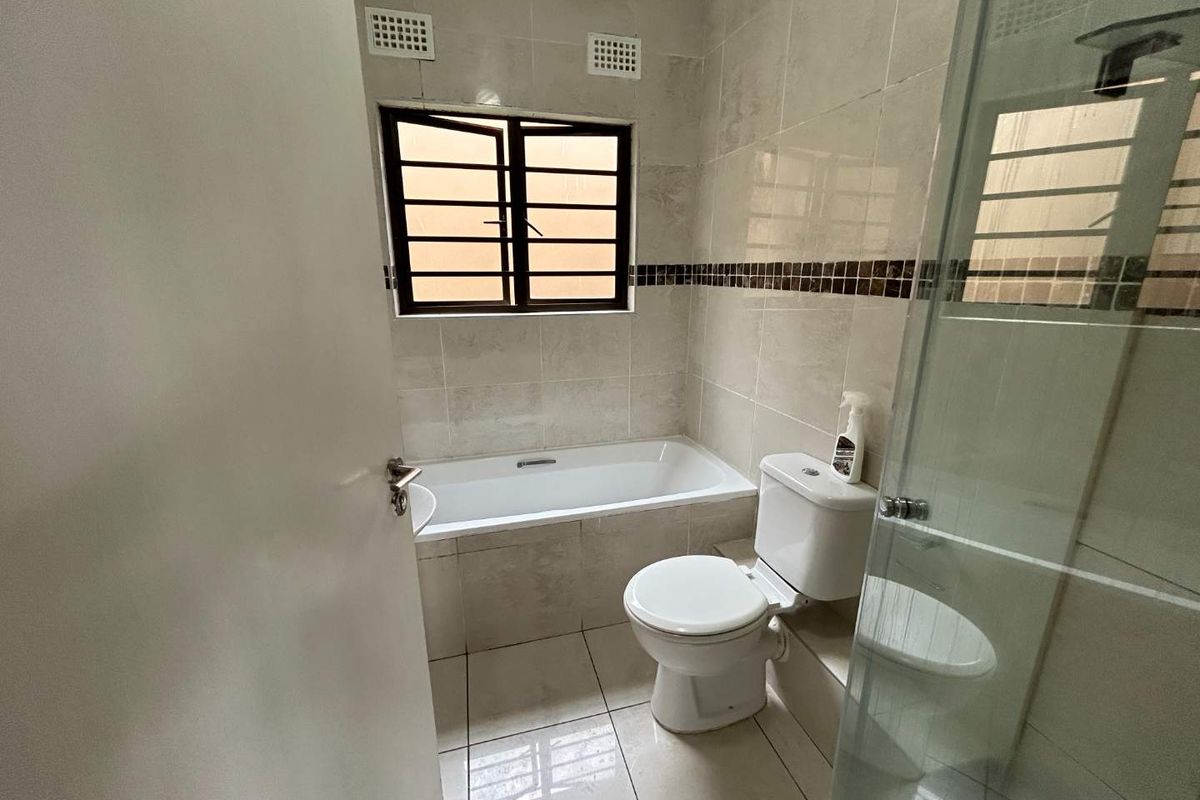 A clean, functional bathroom featuring a built-in bathtub, a separate glass-enclosed shower, and neutral tiled finishes throughout.