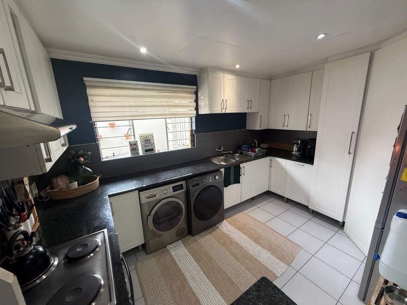 A functional kitchen featuring white cabinetry, dark countertops, tiled flooring, and integrated laundry appliances, offering a clean and practical workspace.