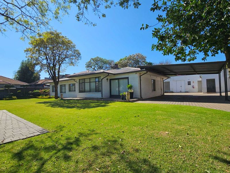 A well-maintained rear exterior view of the house featuring a spacious lawn, paved driveway, and a covered carport area.