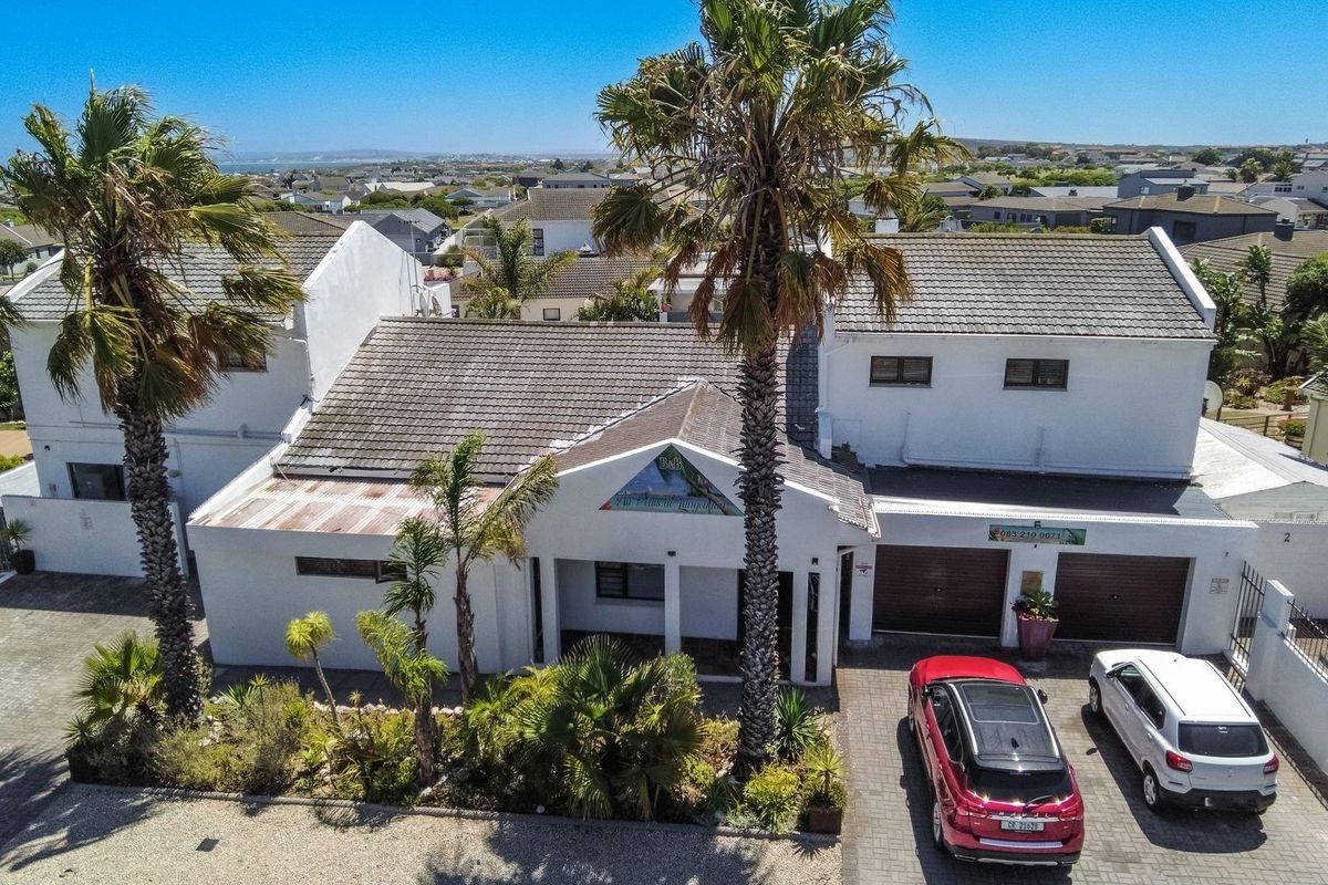 Aerial view of the guest house property featuring a tiled roof, double garage, paved driveway, and established palm trees in a coastal residential setting.