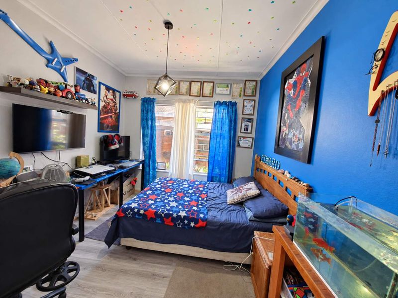 A bedroom featuring laminate flooring, a central pendant light, and a window, currently styled with vibrant decor and personal items.