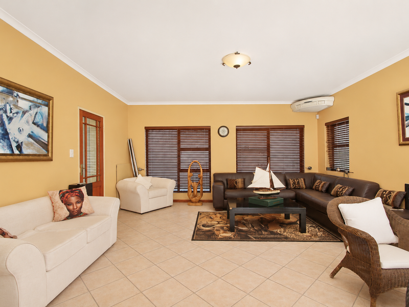 Spacious living room featuring ceramic floor tiles, timber venetian blinds, and a wall-mounted split-system air conditioning unit.