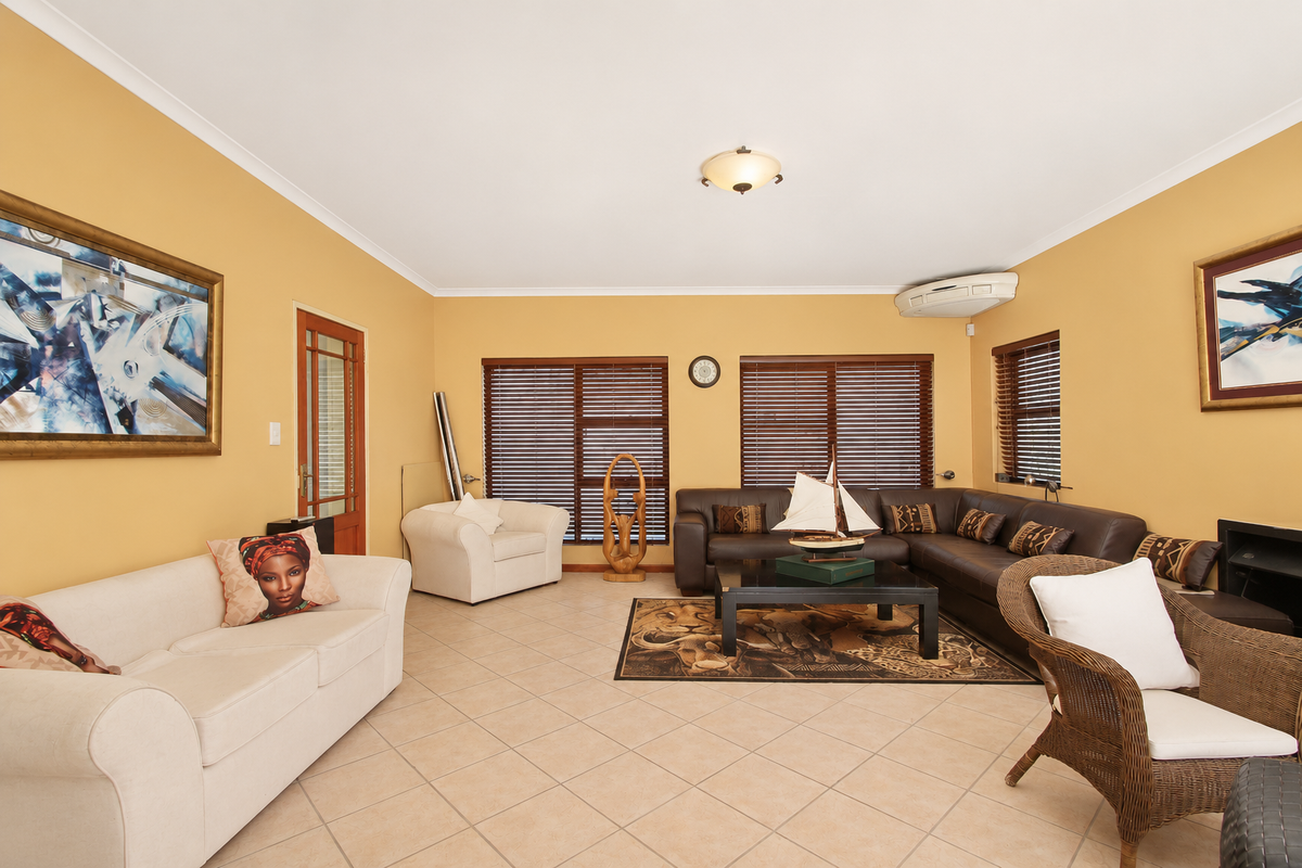 Spacious living room featuring ceramic floor tiles, timber venetian blinds, and a wall-mounted split-system air conditioning unit.