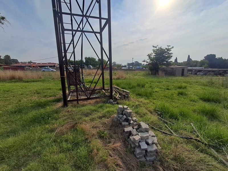 Expansive small holding grounds featuring a metal water tower structure and a small concrete outbuilding set within an open, undeveloped field.