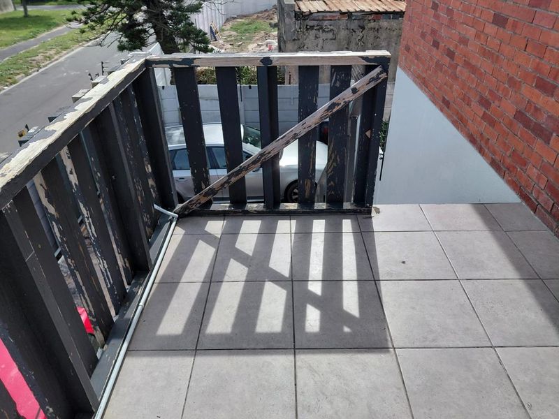 An outdoor balcony area featuring tiled flooring and a timber balustrade that requires maintenance and repainting.