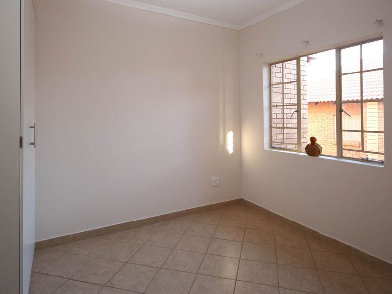A clean, empty bedroom featuring tiled flooring, a built-in wardrobe, and a window with security bars.
