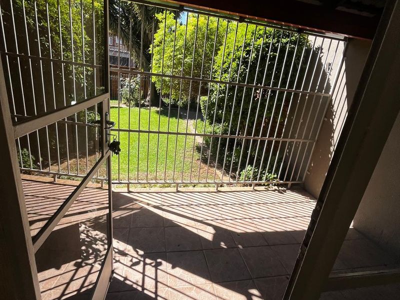 A covered patio area featuring tiled flooring and a security gate, providing direct access to the rear garden.