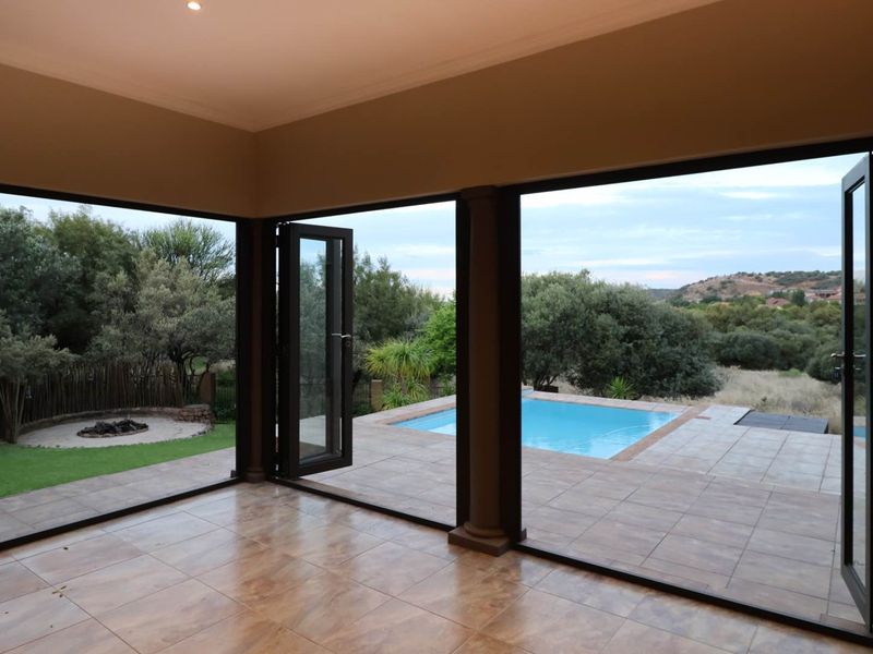 Spacious covered patio featuring large stacking doors that open onto a swimming pool and landscaped garden with a boma area.
