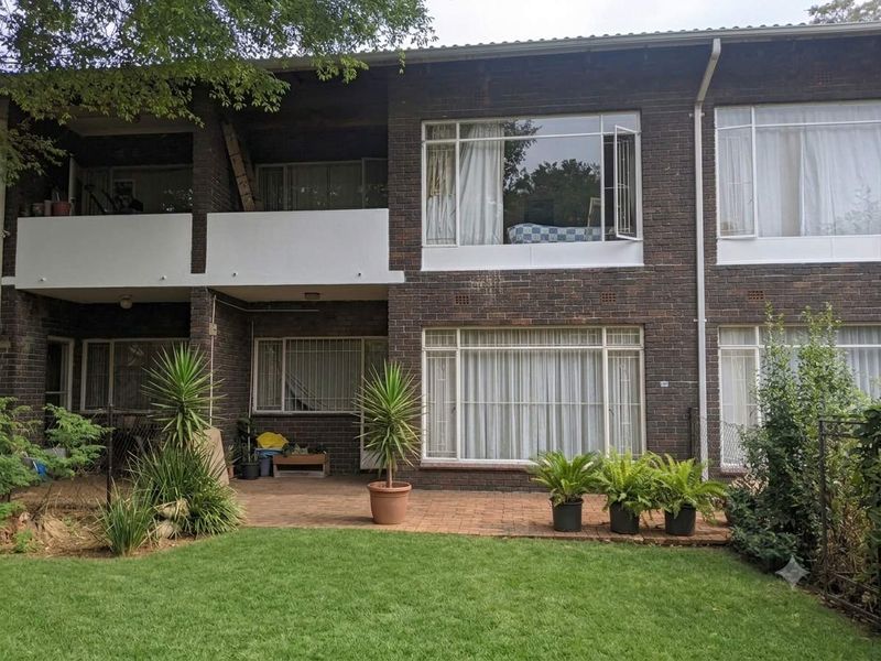 Rear view of a brick apartment building featuring a ground-floor paved patio, a first-floor balcony, and a private garden area.