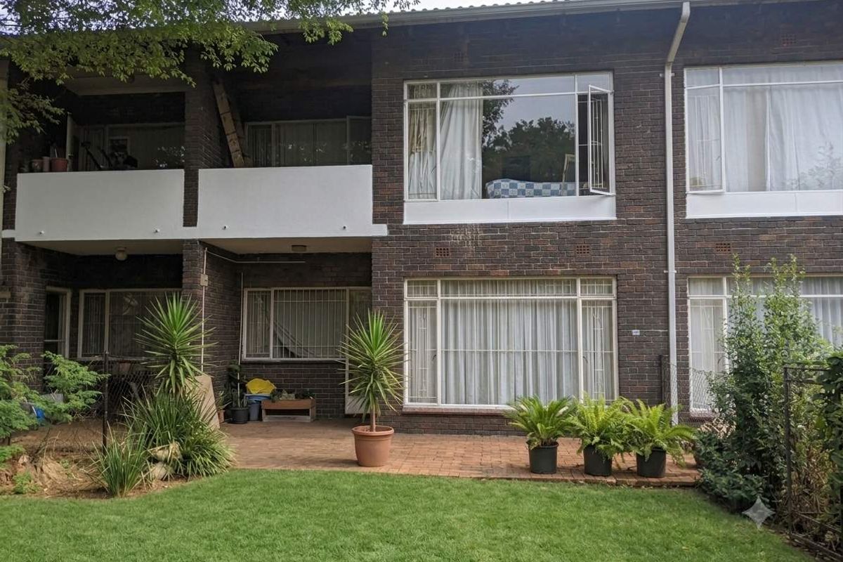 Rear view of a brick apartment building featuring a ground-floor paved patio, a first-floor balcony, and a private garden area.