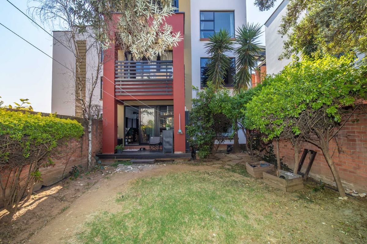 Rear view of the apartment building featuring a private garden, timber deck, and a balcony with modern red facade accents.