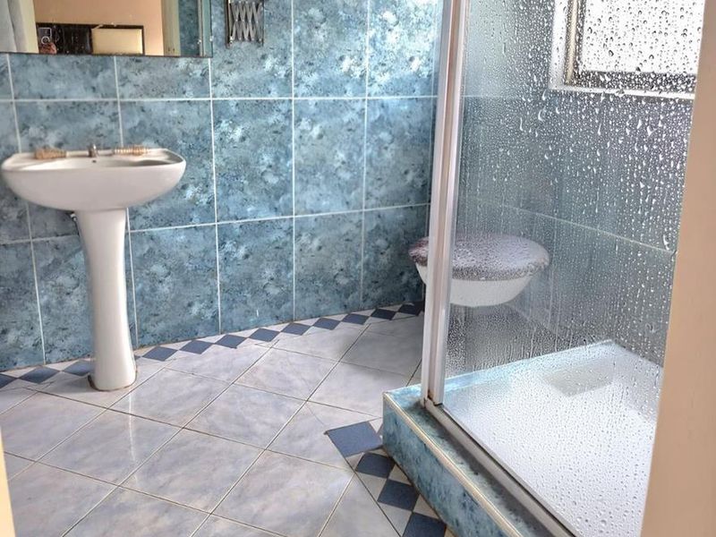 A dated en-suite bathroom featuring a pedestal basin, shower enclosure, and blue patterned wall and floor tiles.