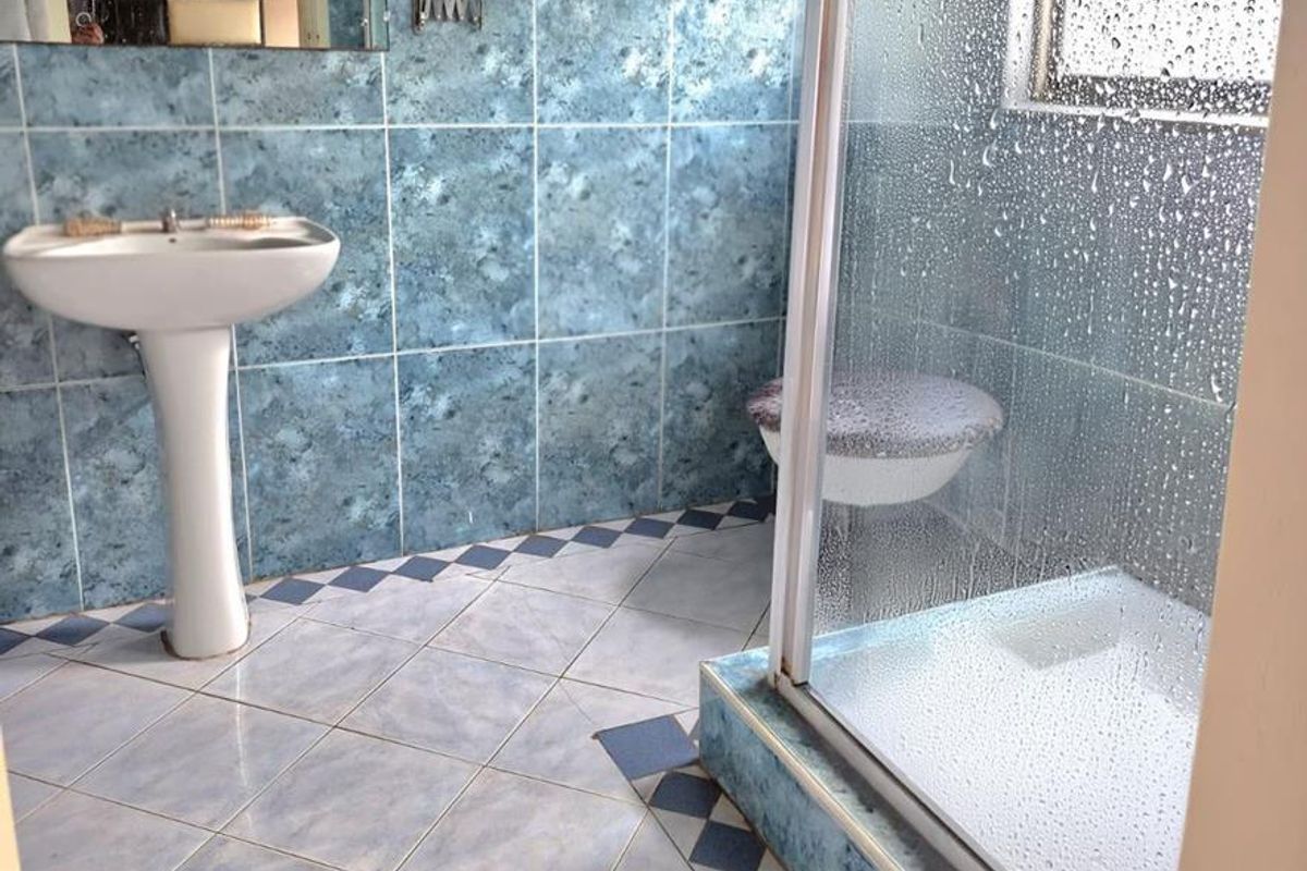 A dated en-suite bathroom featuring a pedestal basin, shower enclosure, and blue patterned wall and floor tiles.