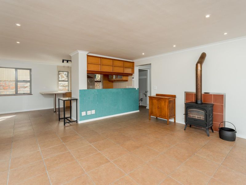 Open-plan living area featuring tiled flooring, recessed lighting, and a prominent wood-burning fireplace, seamlessly connected to a functional kitchen space.