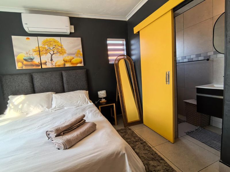 A modern bedroom featuring a bold yellow sliding barn door leading to an en-suite bathroom, tiled flooring, and a wall-mounted air conditioning unit.