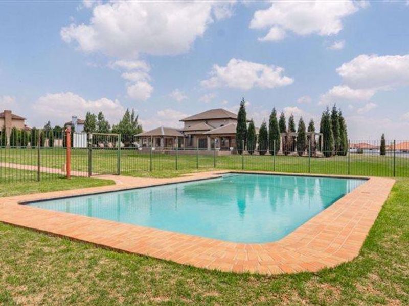 A well-maintained outdoor swimming pool area featuring brick coping and secure metal perimeter fencing, set within a spacious landscaped garden.