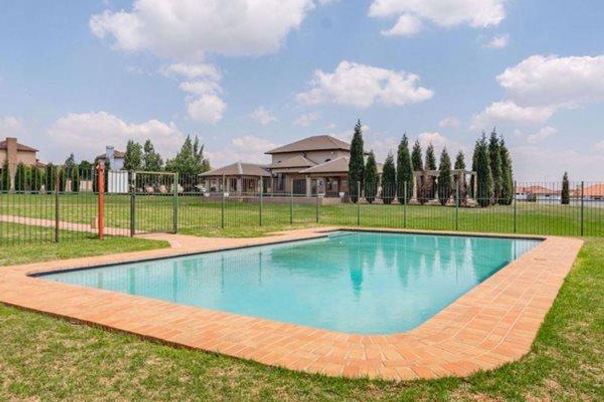 A well-maintained outdoor swimming pool area featuring brick coping and secure metal perimeter fencing, set within a spacious landscaped garden.