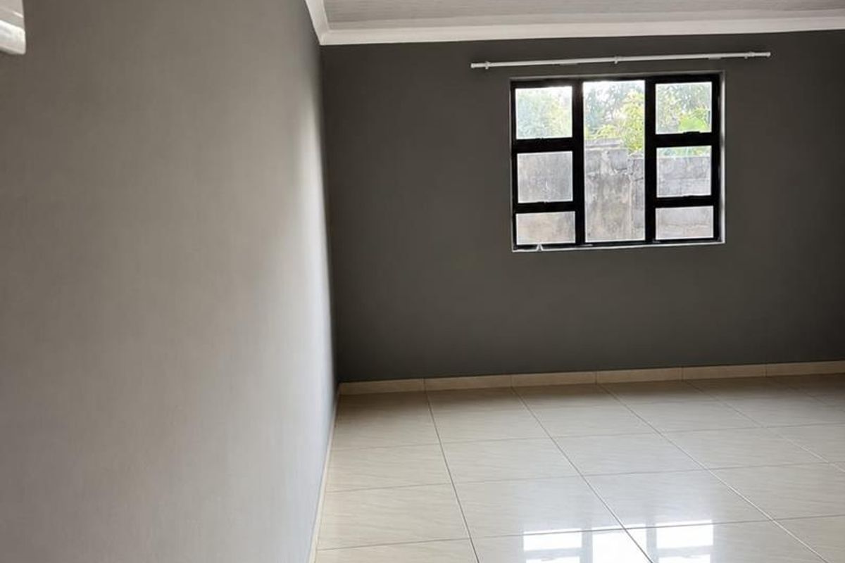 A bright, empty bedroom featuring neutral grey walls, polished tiled flooring, and modern recessed lighting, providing a clean and versatile living space.