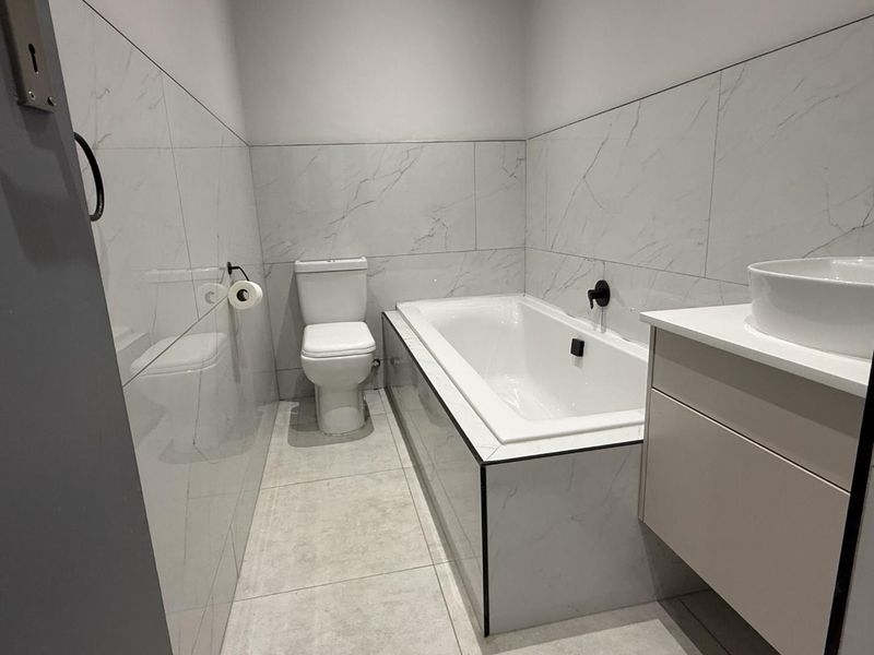 Modern bathroom featuring marble-look wall tiles, a built-in bathtub, a sleek vanity with a vessel sink, and contemporary black fixtures.