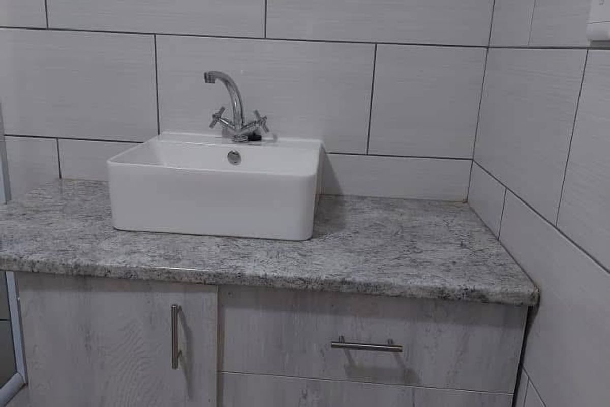 A modern bathroom vanity featuring a white ceramic vessel sink, granite-look countertop, and light wood-grain cabinetry with tiled walls.