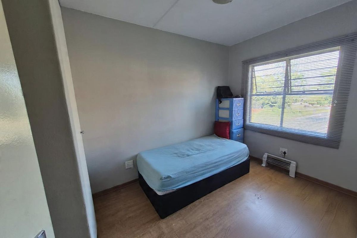 A compact bedroom featuring laminate flooring, a window with fitted blinds, and a ceiling light fixture.