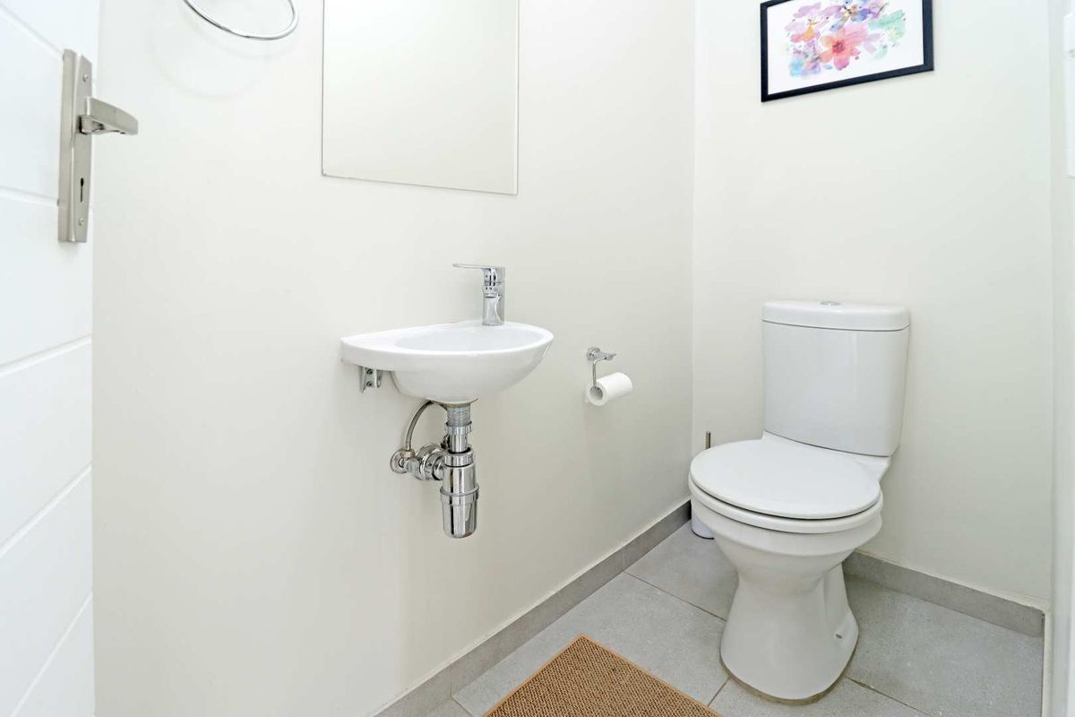 A clean and functional guest powder room featuring a wall-mounted basin, chrome tapware, and a modern toilet suite.