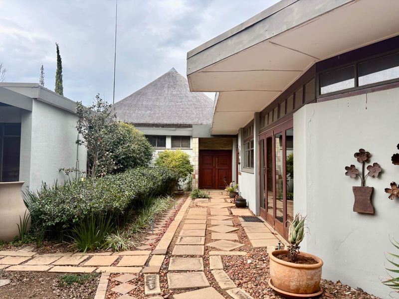 A front entrance pathway featuring stone paving, leading to double timber doors with a distinctive thatched roof structure in the background.
