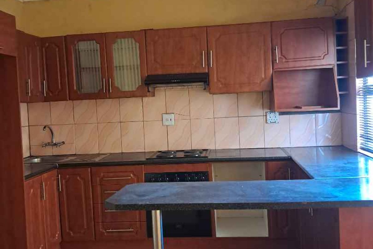 A dated kitchen featuring wooden cabinetry, a built-in hob and oven, tiled splashbacks, and a breakfast bar counter.