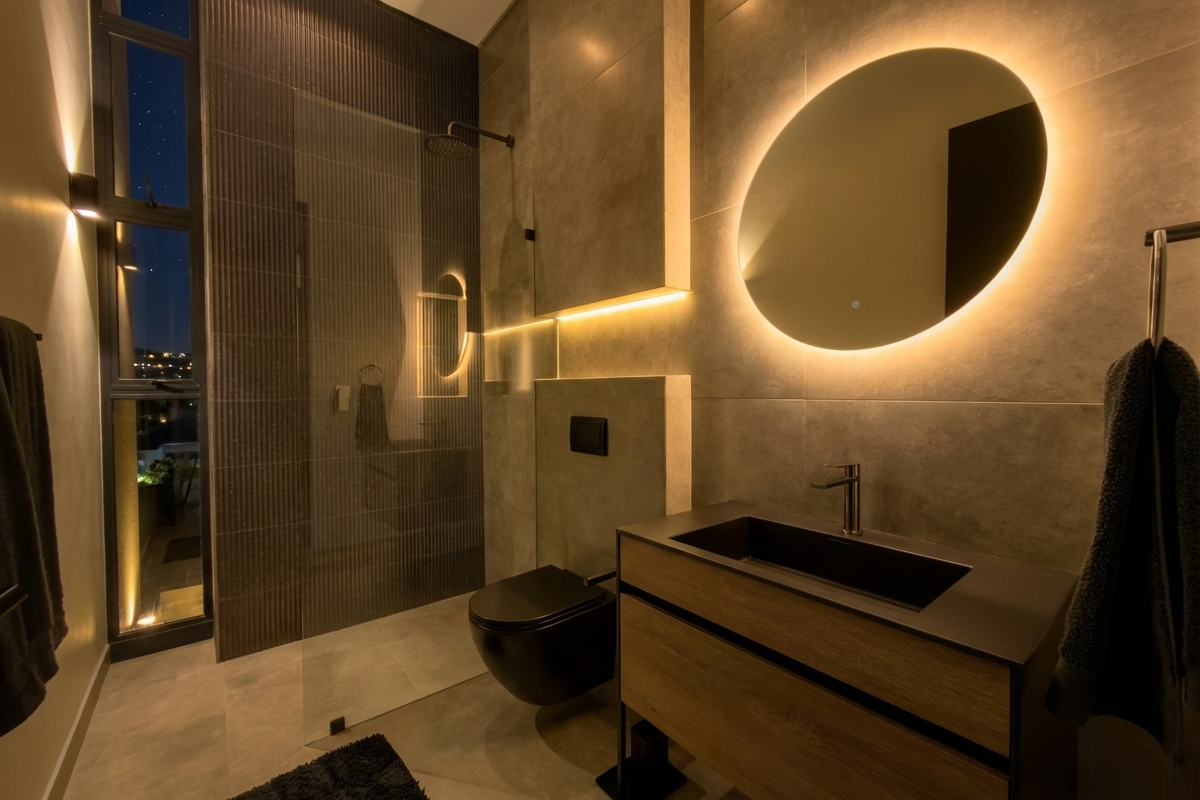 Modern bathroom featuring a walk-in shower with glass partition, wall-mounted toilet, and a sleek vanity with integrated basin and backlit mirror.