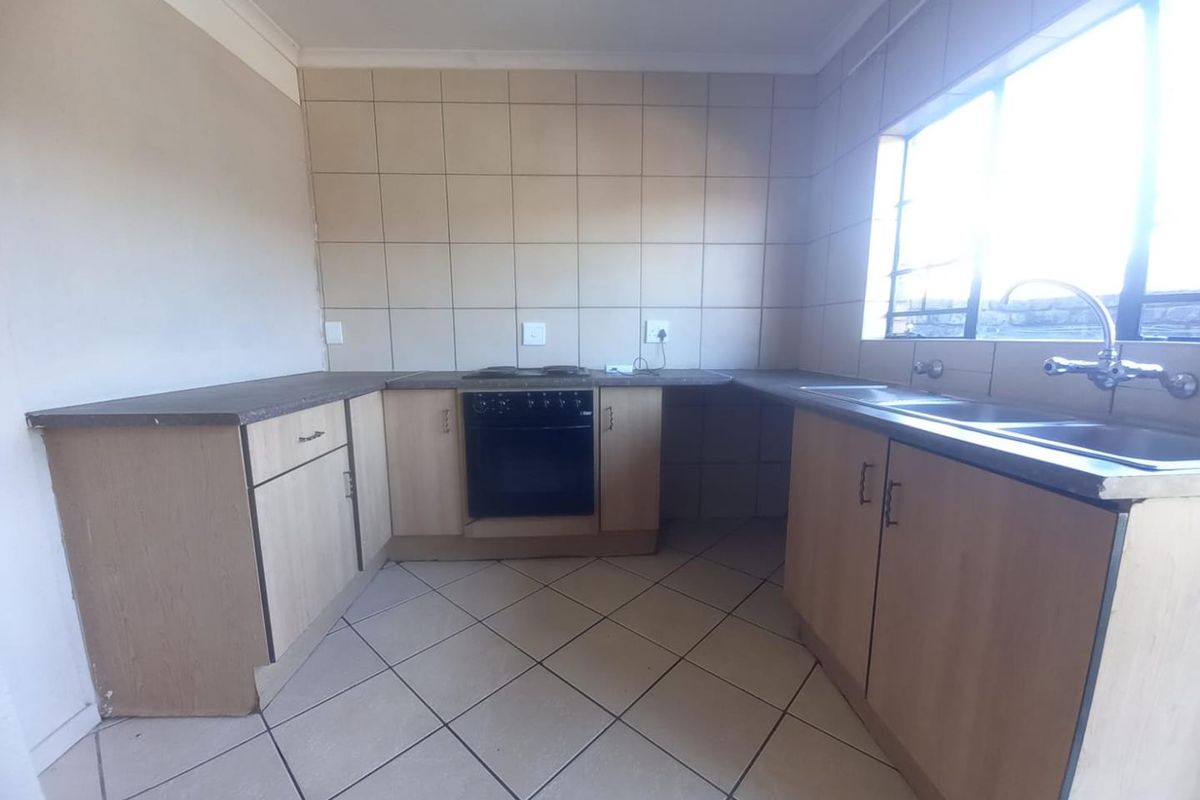 A functional kitchen featuring light wood-tone cabinetry, tiled splashbacks, a built-in oven and hob, and a double stainless steel sink.