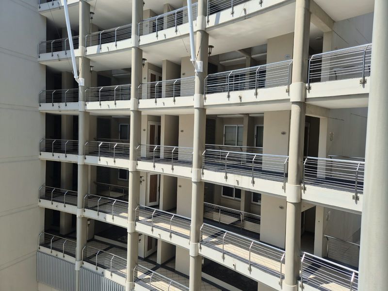 A multi-level apartment building facade featuring stacked balconies with stainless steel railings and concrete support columns.