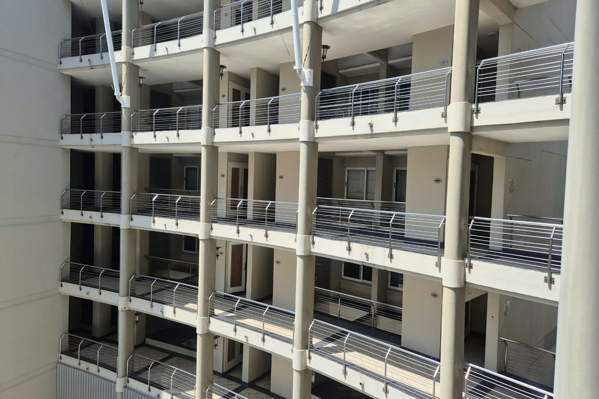 A multi-level apartment building facade featuring stacked balconies with stainless steel railings and concrete support columns.