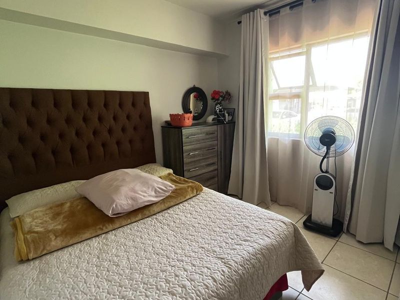 A functional bedroom featuring tiled flooring, neutral wall finishes, and a window with curtain tracks, providing a comfortable living space.