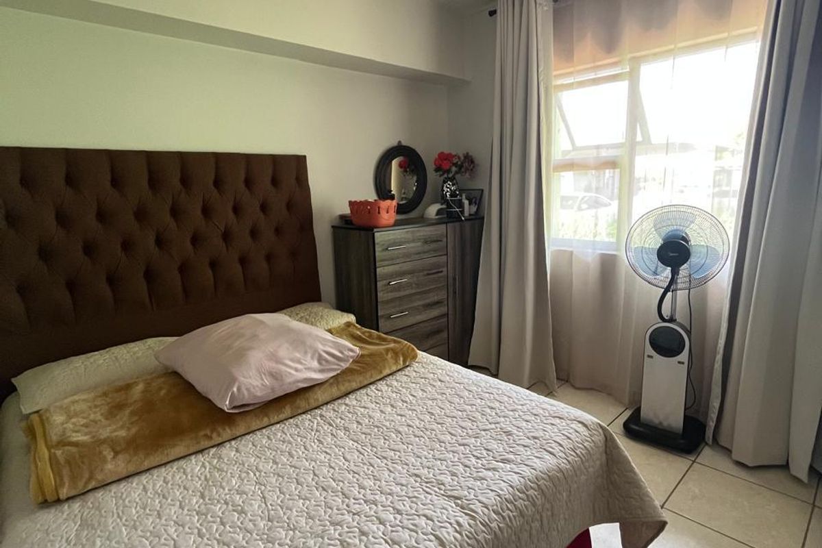 A functional bedroom featuring tiled flooring, neutral wall finishes, and a window with curtain tracks, providing a comfortable living space.