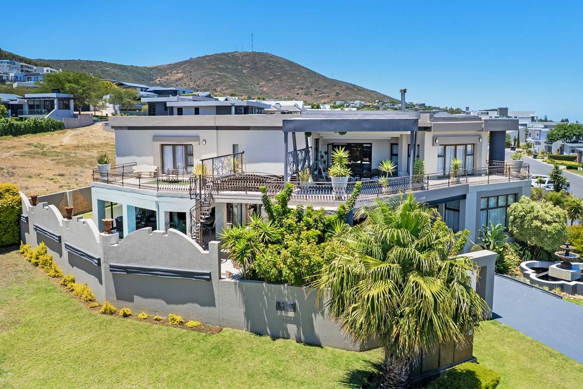 Aerial view of a modern multi-level residence featuring an expansive upper balcony, wrought iron railings, a spiral staircase, and a landscaped garden with water feature.