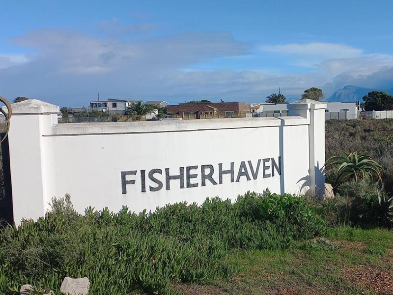 A view of the Fisherhaven entrance signage and boundary wall, situated in a residential area with surrounding natural vegetation.