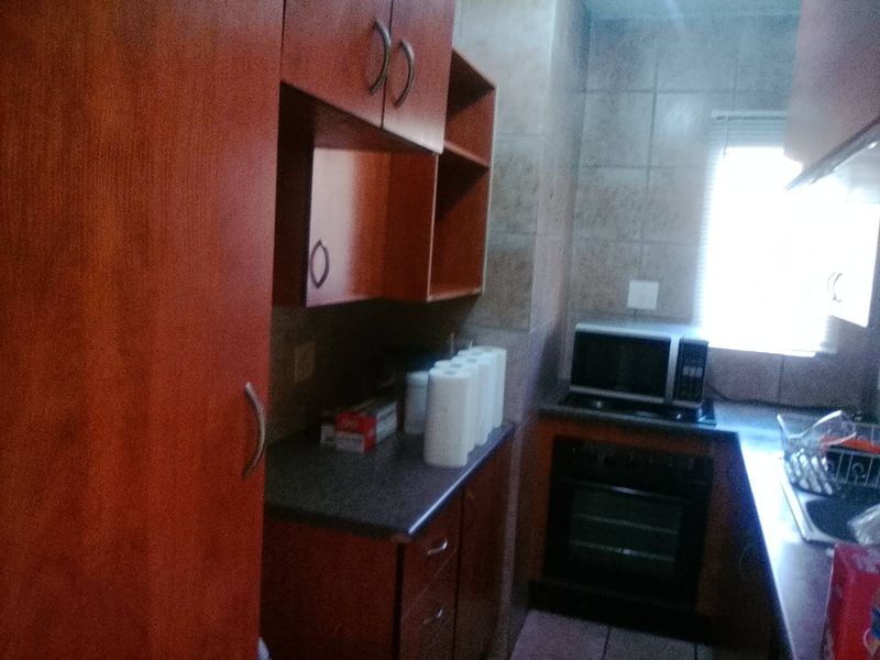 A compact kitchen featuring wooden cabinetry, built-in oven, microwave, and tiled backsplash, offering functional storage and preparation space.