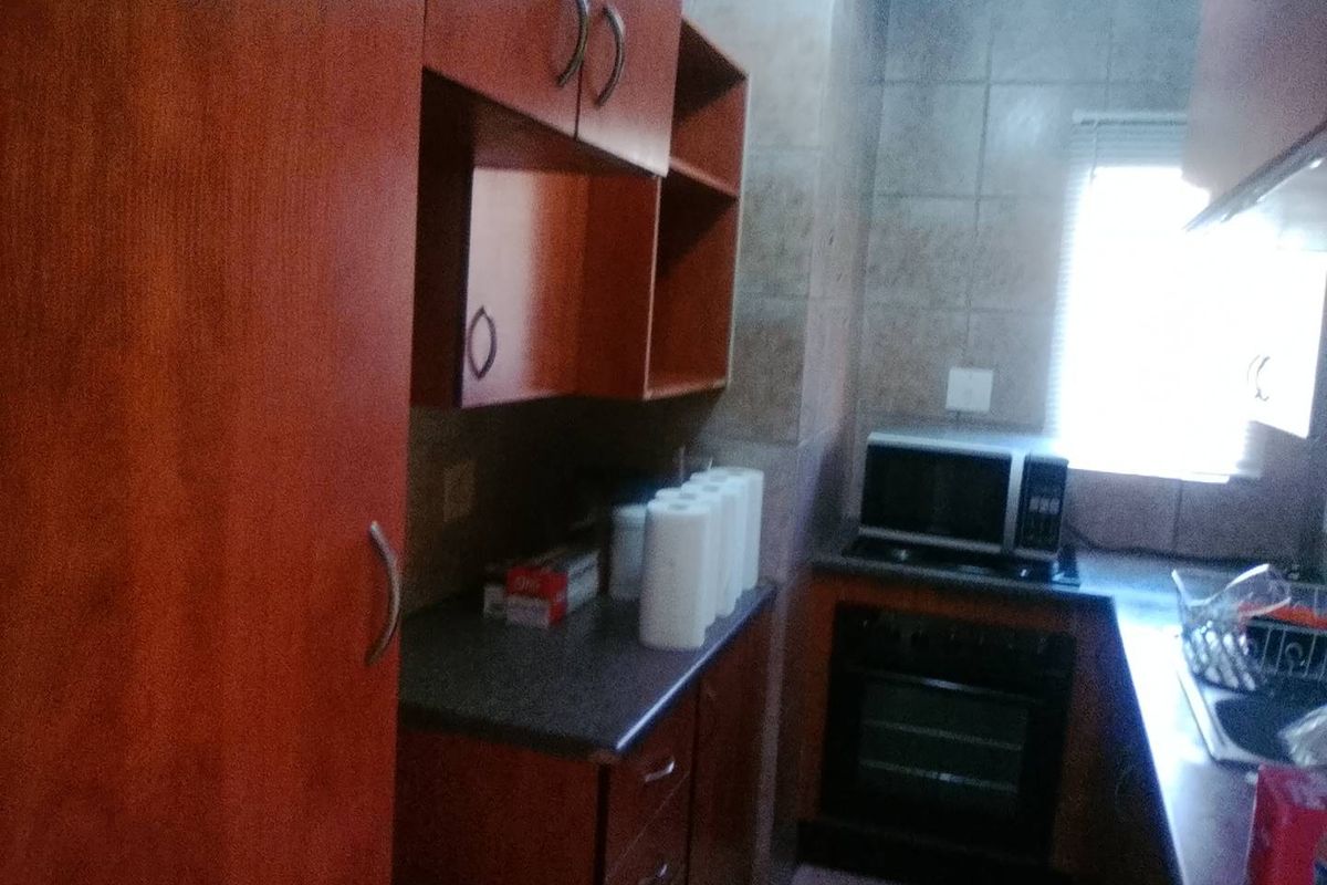 A compact kitchen featuring wooden cabinetry, built-in oven, microwave, and tiled backsplash, offering functional storage and preparation space.