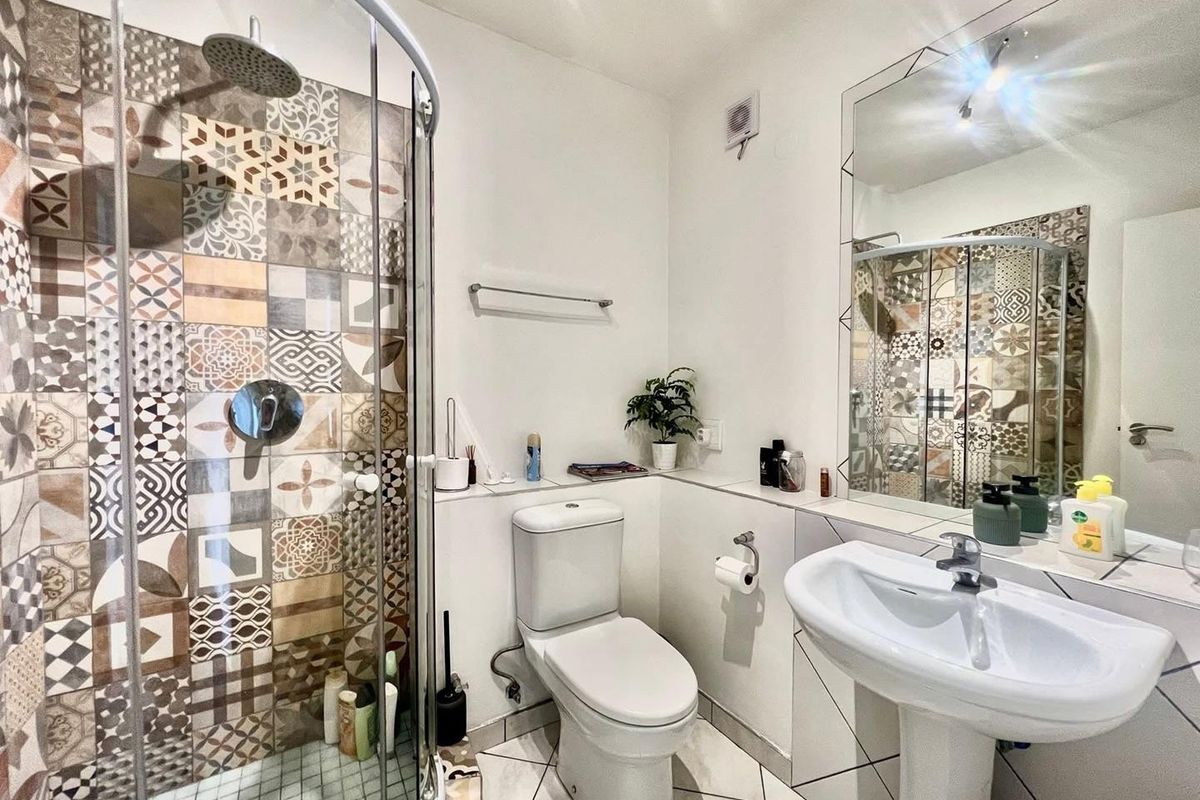 Modern bathroom featuring a curved glass shower enclosure with decorative patterned tiles, a pedestal basin, and a large wall-mounted mirror.