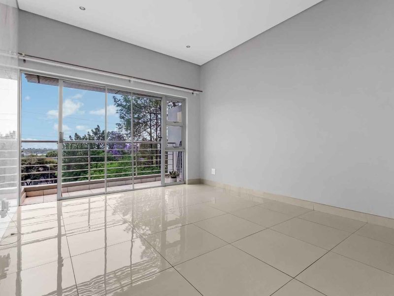 Bright and spacious living area featuring large sliding glass doors that open onto a balcony, complemented by neutral tiled flooring and recessed lighting.