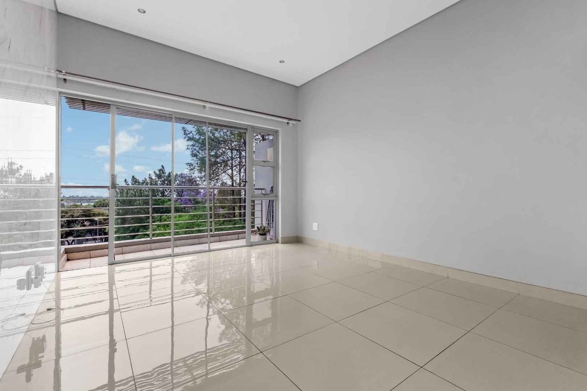 Bright and spacious living area featuring large sliding glass doors that open onto a balcony, complemented by neutral tiled flooring and recessed lighting.