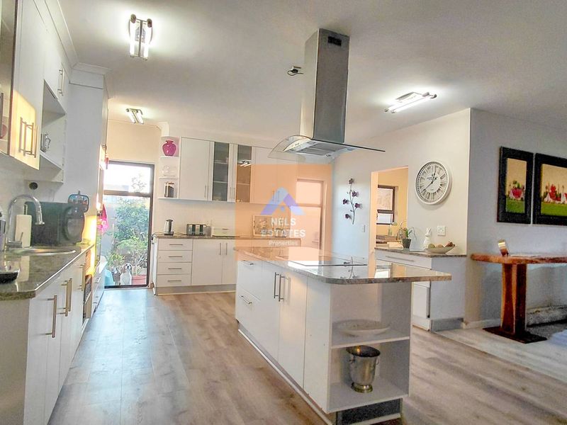 Modern open-plan kitchen featuring a central island with granite countertops, sleek white cabinetry, and high-quality laminate flooring, seamlessly connecting to the living area.