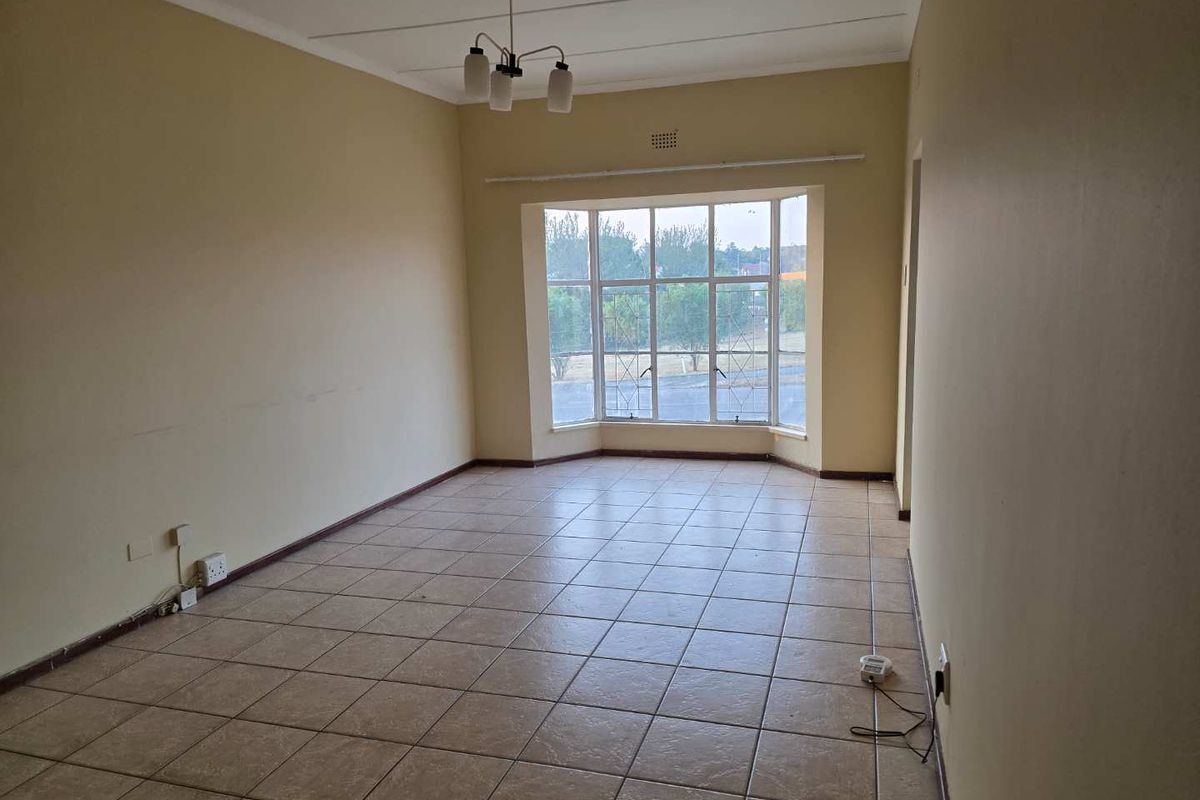 A spacious, empty living room featuring tiled flooring, a large bay window, and a central ceiling light fixture.