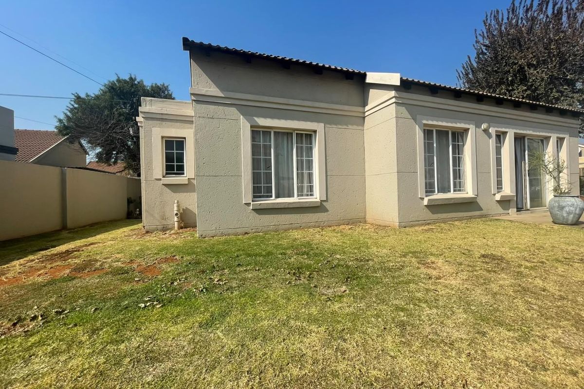 Rear view of the house featuring plastered walls, tiled roof, and sliding glass doors opening onto a lawn area.