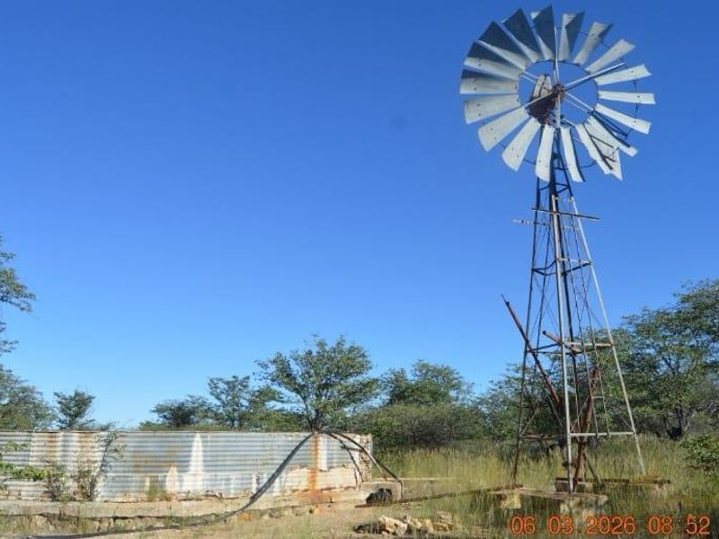 A rural farm scene featuring a traditional metal windmill and a corrugated iron water storage tank set in an open field.