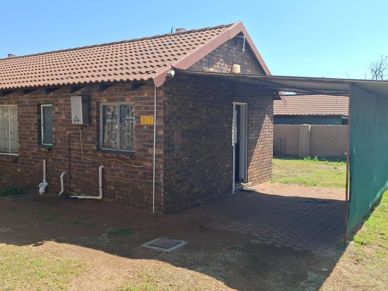 A single-story face brick house featuring a tiled roof, attached carport, and paved driveway area.