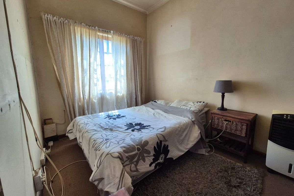A bedroom featuring carpeted flooring and window treatments, currently requiring cosmetic updates to the wall finishes and electrical fixtures.
