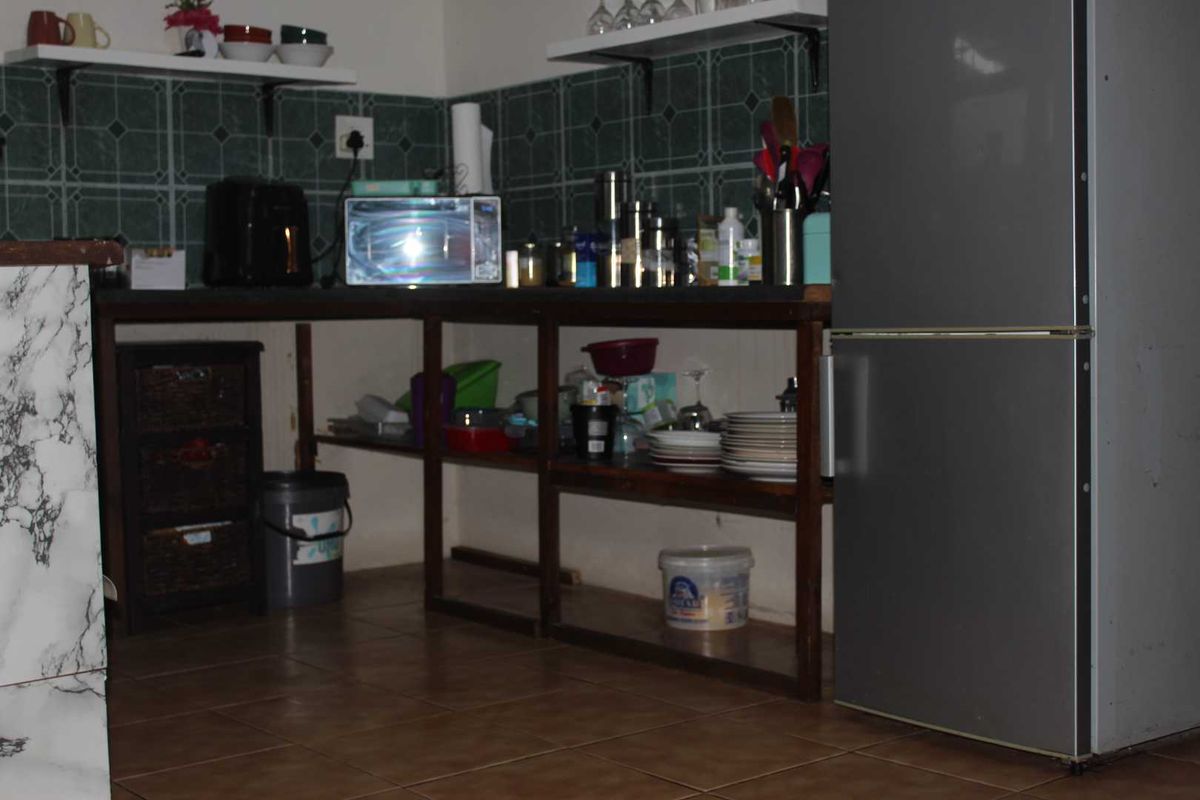 A kitchen area featuring open shelving, tiled backsplash, and tiled flooring, currently showing dated finishes and requiring modernization.
