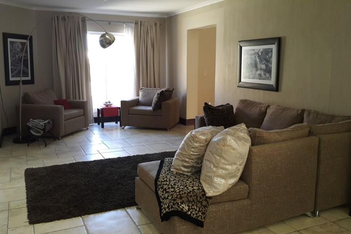 A spacious living room featuring neutral-toned walls, tiled flooring, and large windows that provide natural light.